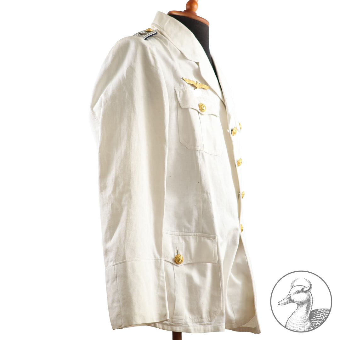 Weißes Jackett (nach neuer Vorschrift) der Kriegsmarine für einen Leutnant der
Küstenartillerie . Das Jackett besitzt aufgesetzte Brust- und Seitentaschen mit Quetschfalten. Die
feuervergoldeten Ankerknöpfe sind sicher mit Sprengringen angebracht, während der
vorschriftsmäßige Metallbrustadler mittels typischer Zwirnschlaufen befestigt ist. Innen finden sich ein Größen- und Herstellerstempel sowie die Namensstickerei
„Hadenfeld“