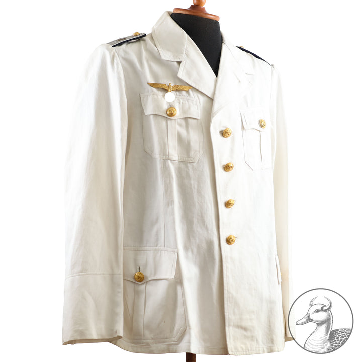 Weißes Jackett (nach neuer Vorschrift) der Kriegsmarine für einen Leutnant der
Küstenartillerie . Das Jackett besitzt aufgesetzte Brust- und Seitentaschen mit Quetschfalten. Die
feuervergoldeten Ankerknöpfe sind sicher mit Sprengringen angebracht, während der
vorschriftsmäßige Metallbrustadler mittels typischer Zwirnschlaufen befestigt ist. Innen finden sich ein Größen- und Herstellerstempel sowie die Namensstickerei
„Hadenfeld“