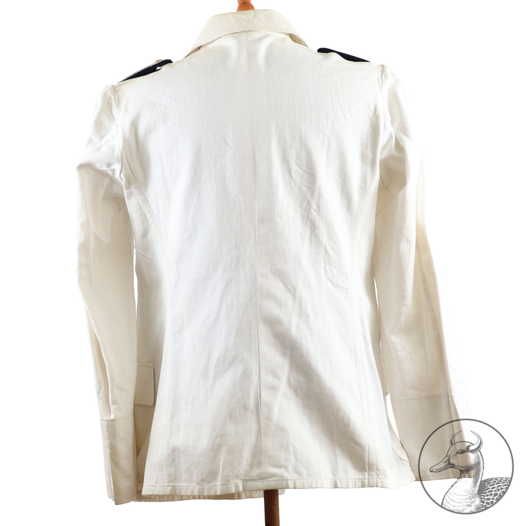 Weißes Jackett (nach neuer Vorschrift) der Kriegsmarine für einen Leutnant der
Küstenartillerie . Das Jackett besitzt aufgesetzte Brust- und Seitentaschen mit Quetschfalten. Die
feuervergoldeten Ankerknöpfe sind sicher mit Sprengringen angebracht, während der
vorschriftsmäßige Metallbrustadler mittels typischer Zwirnschlaufen befestigt ist. Innen finden sich ein Größen- und Herstellerstempel sowie die Namensstickerei
„Hadenfeld“