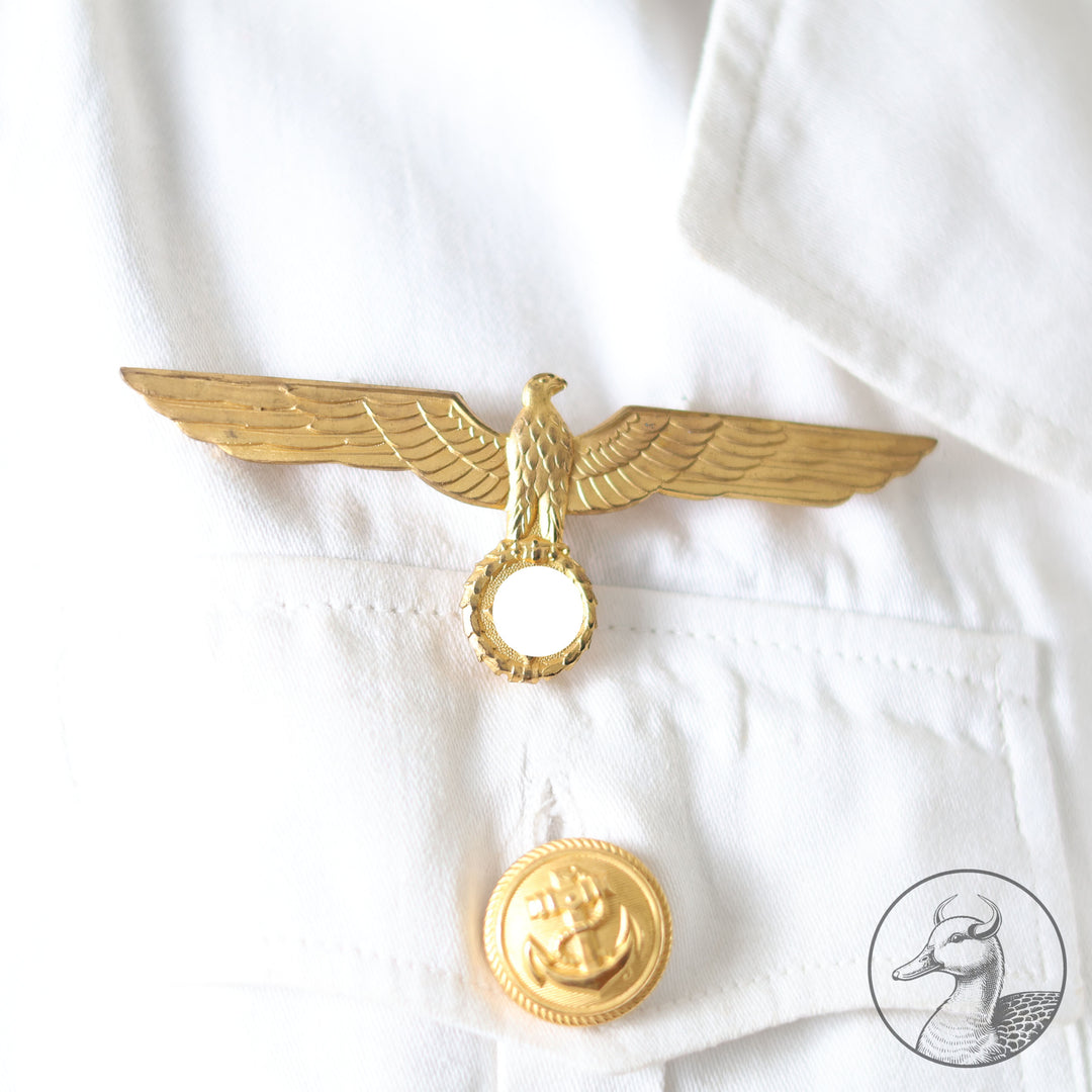 Weißes Jackett (nach neuer Vorschrift) der Kriegsmarine für einen Leutnant der
Küstenartillerie . Das Jackett besitzt aufgesetzte Brust- und Seitentaschen mit Quetschfalten. Die
feuervergoldeten Ankerknöpfe sind sicher mit Sprengringen angebracht, während der
vorschriftsmäßige Metallbrustadler mittels typischer Zwirnschlaufen befestigt ist. Innen finden sich ein Größen- und Herstellerstempel sowie die Namensstickerei
„Hadenfeld“