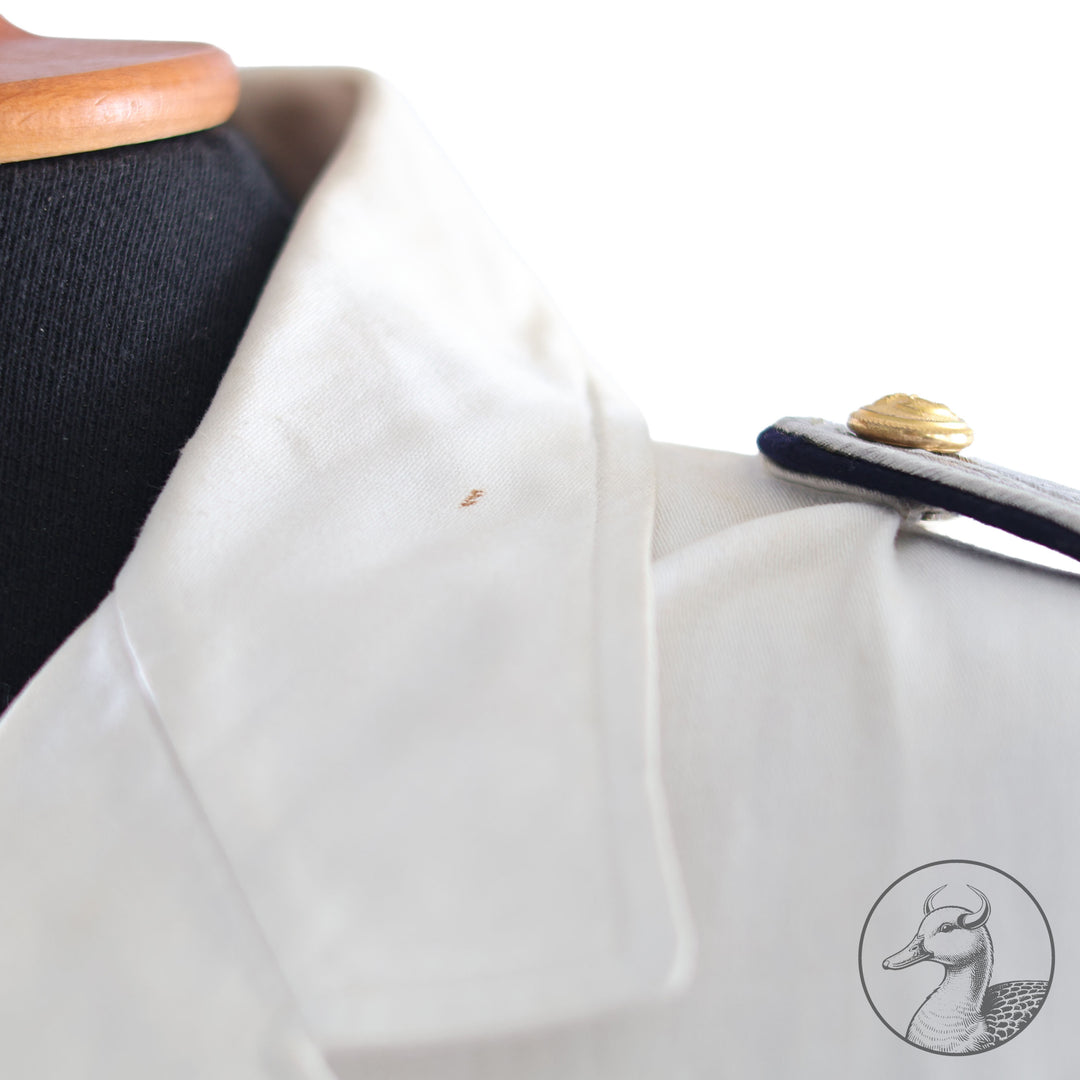 Weißes Jackett (nach neuer Vorschrift) der Kriegsmarine für einen Leutnant der
Küstenartillerie . Das Jackett besitzt aufgesetzte Brust- und Seitentaschen mit Quetschfalten. Die
feuervergoldeten Ankerknöpfe sind sicher mit Sprengringen angebracht, während der
vorschriftsmäßige Metallbrustadler mittels typischer Zwirnschlaufen befestigt ist. Innen finden sich ein Größen- und Herstellerstempel sowie die Namensstickerei
„Hadenfeld“