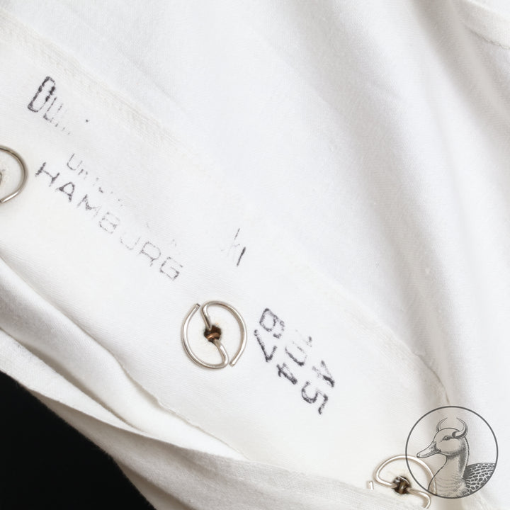 Weißes Jackett (nach neuer Vorschrift) der Kriegsmarine für einen Leutnant der
Küstenartillerie . Das Jackett besitzt aufgesetzte Brust- und Seitentaschen mit Quetschfalten. Die
feuervergoldeten Ankerknöpfe sind sicher mit Sprengringen angebracht, während der
vorschriftsmäßige Metallbrustadler mittels typischer Zwirnschlaufen befestigt ist. Innen finden sich ein Größen- und Herstellerstempel sowie die Namensstickerei
„Hadenfeld“